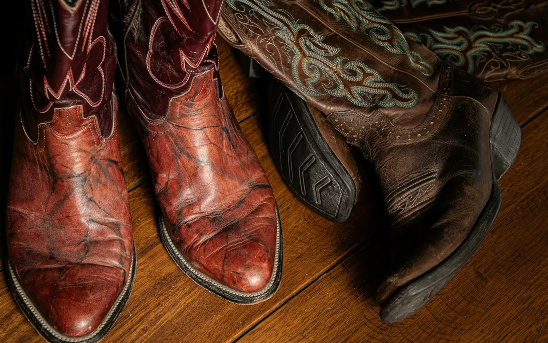Two pairs of worn leather cowboy boots on a wooden floor