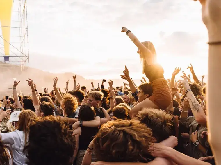 A festival crowd at sunset with their arms in the air